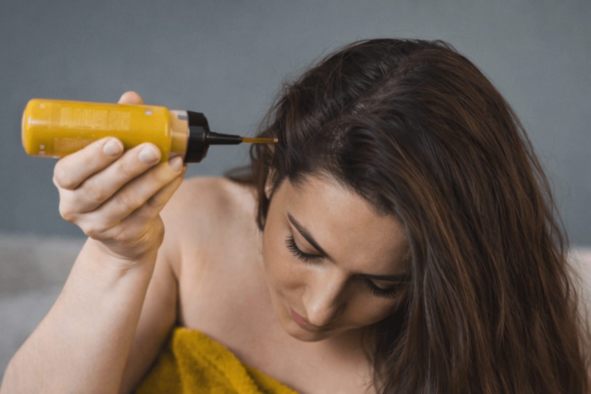 Woman applying a hair growth mask directly to her scalp before shampooing