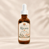 An amber glass bottle of Rivara Scalp Oil with a white dropper cap, centered against a warm beige background with soft leaf shadows.